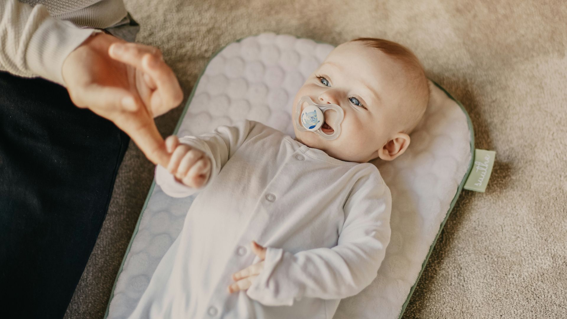 baby in white onesie lying on white textile