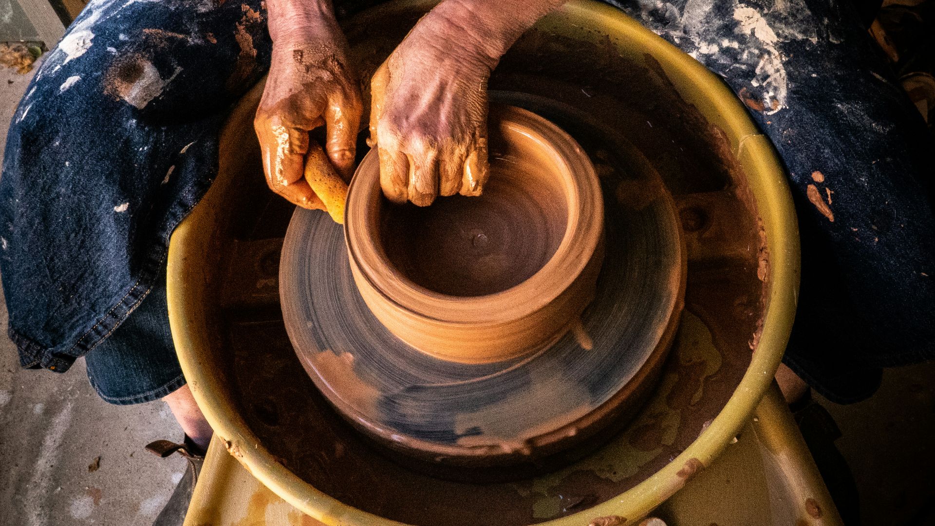 person in blue denim jeans making clay pot