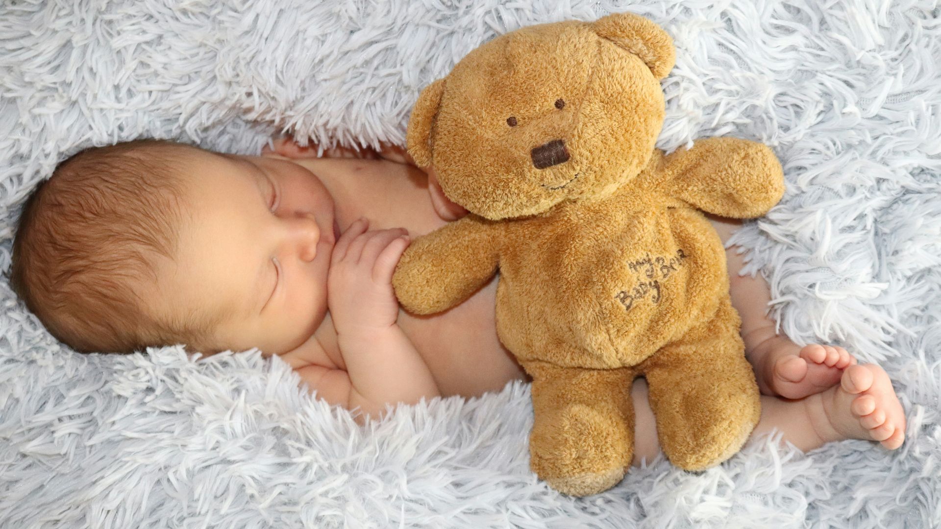 baby lying on white fur textile beside brown bear plush toy