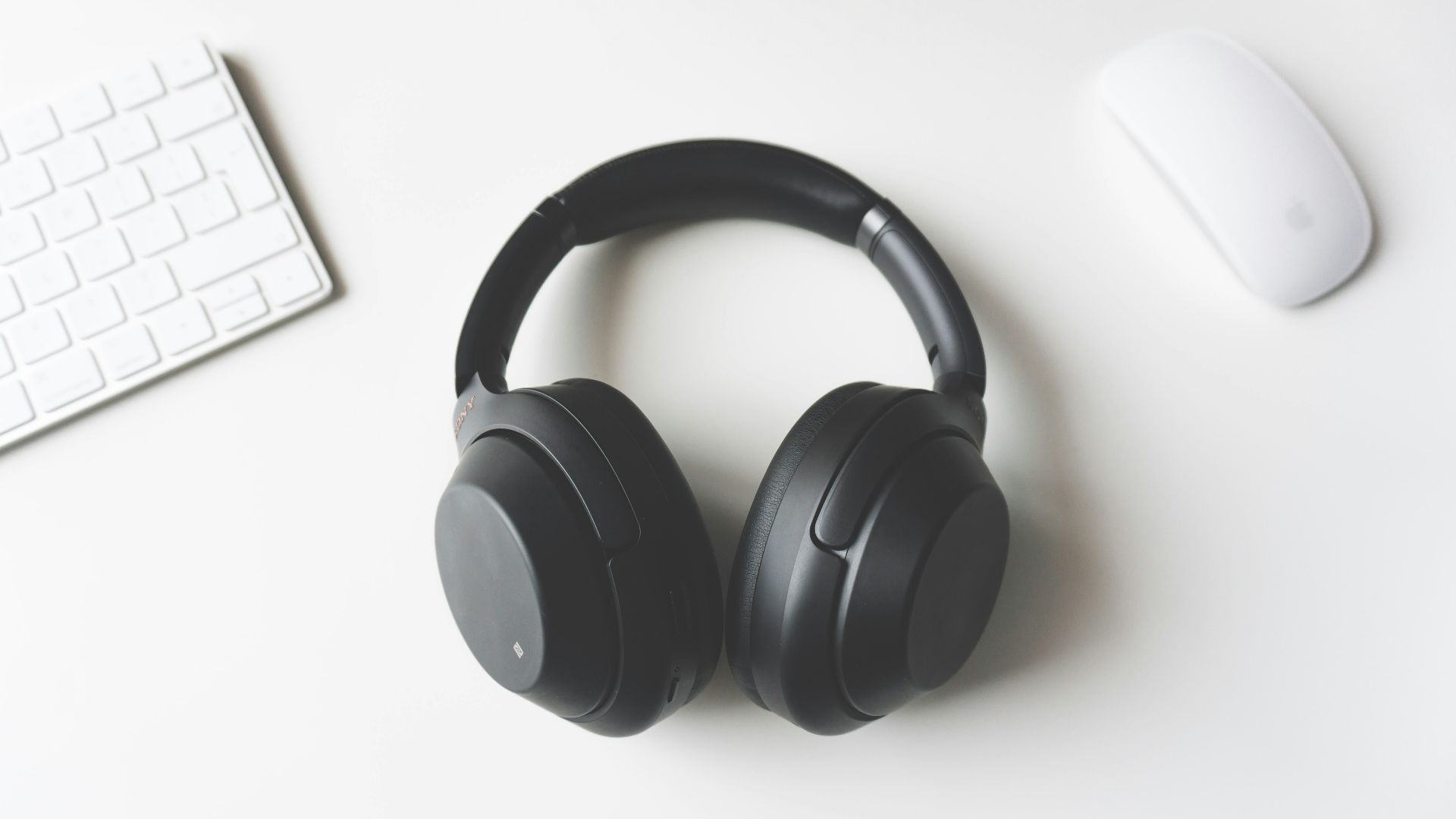 black wireless headphones between Apple Keyboard and Apple Magic Mouse on white surface