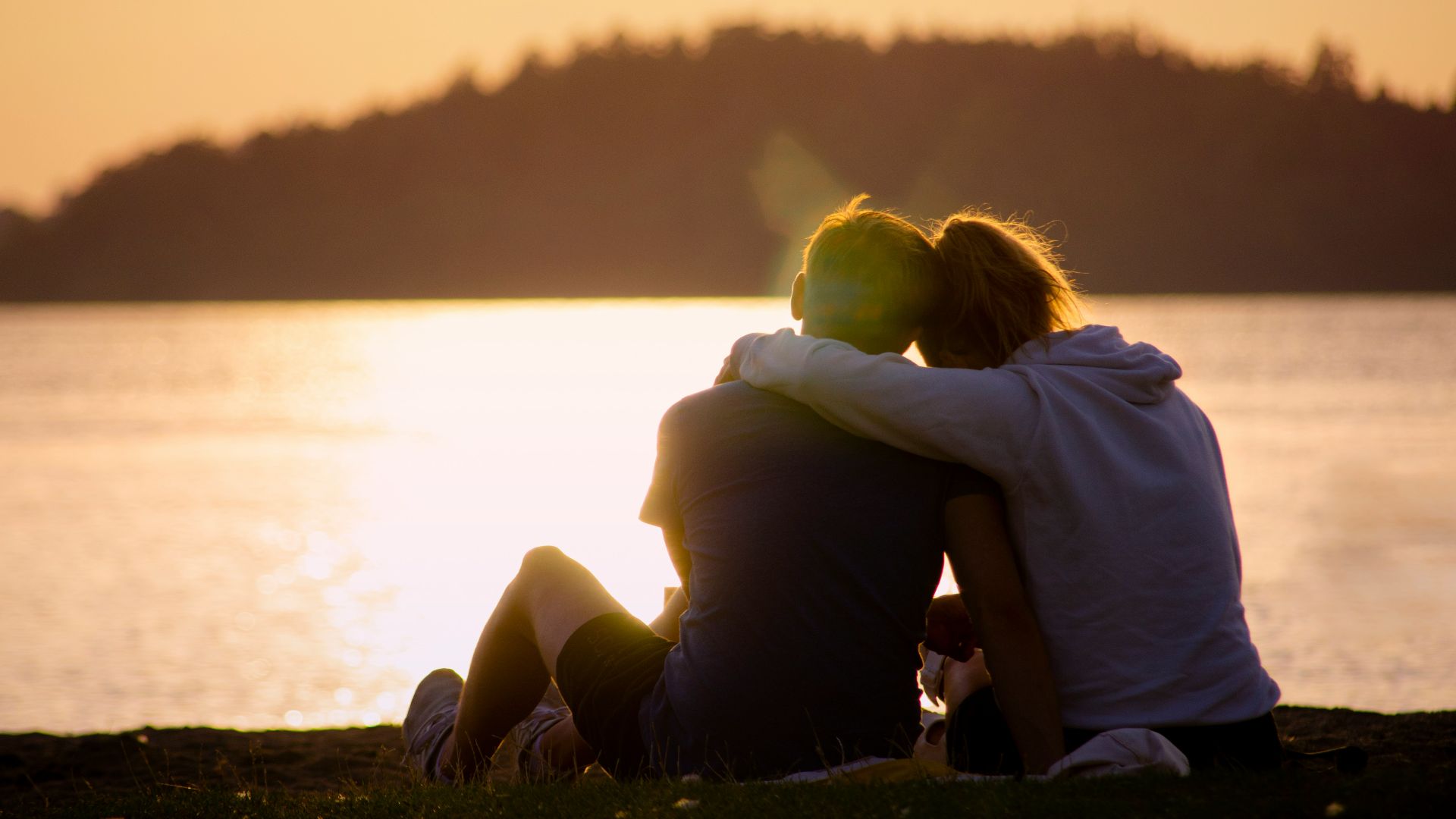 woman in black jacket sitting on green grass field near body of water during daytime