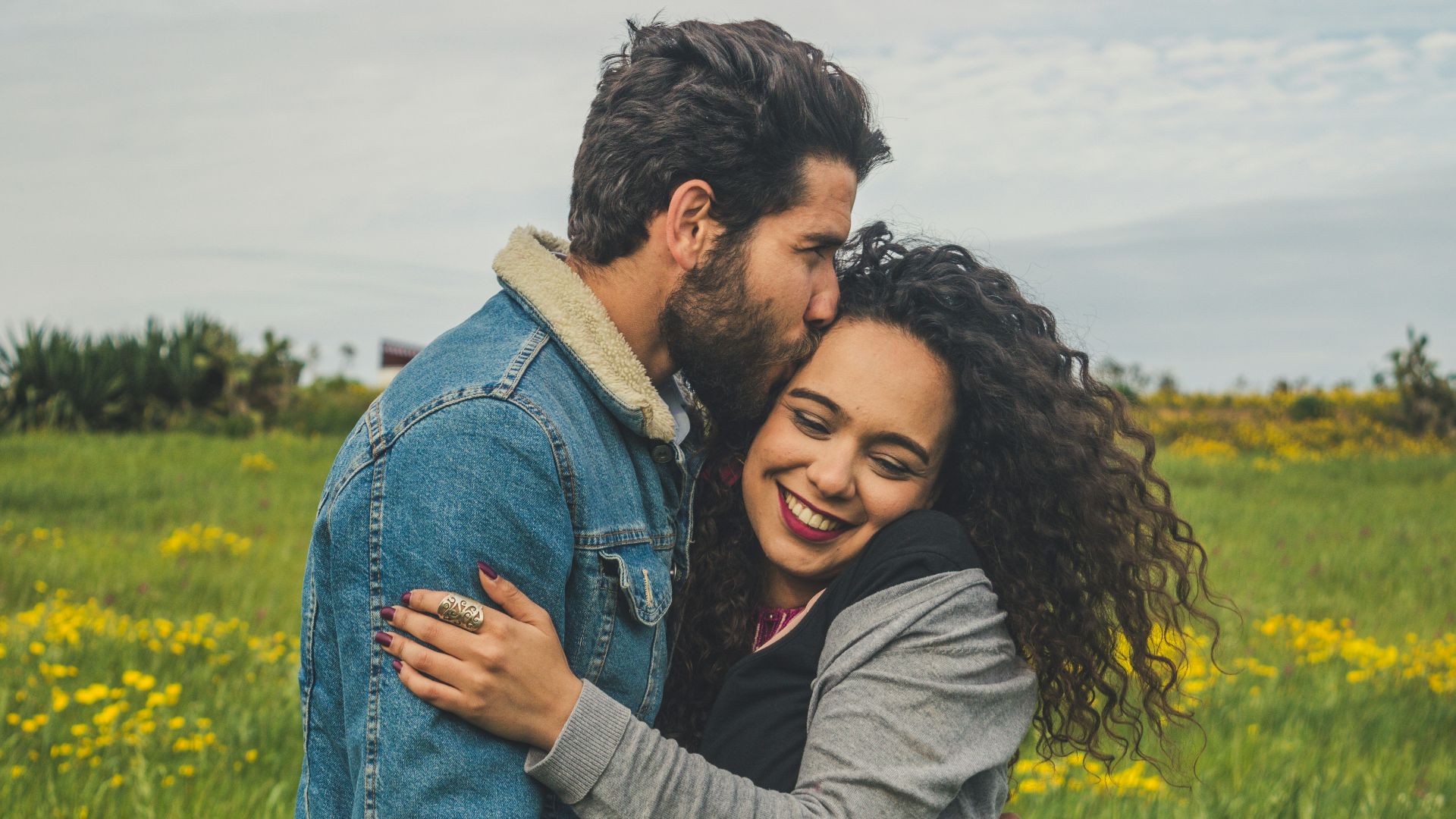 man kissing on woman's head on the green grassy field