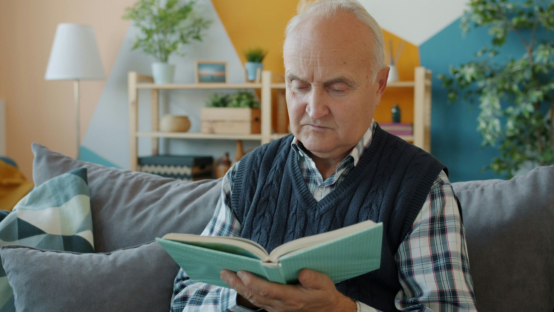 Elderly man reading a book on a couch.