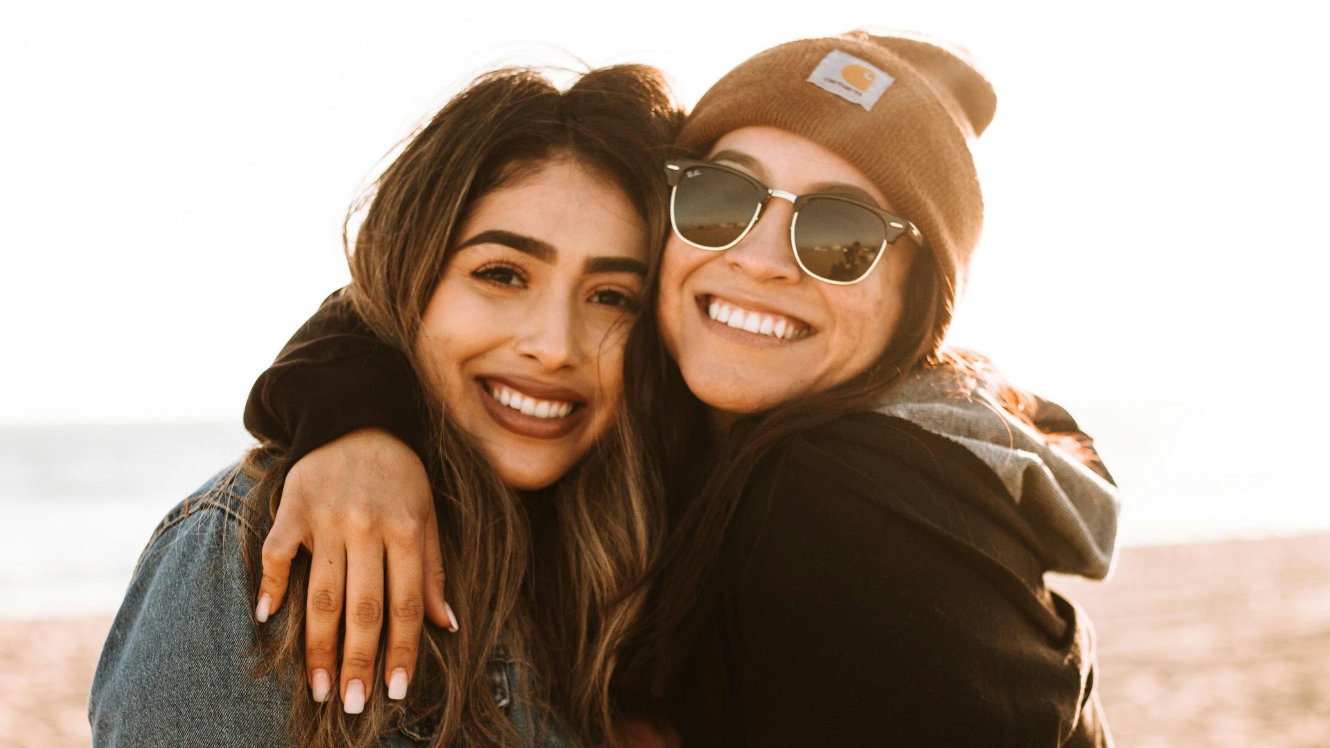 woman hugging other woman while smiling at beach