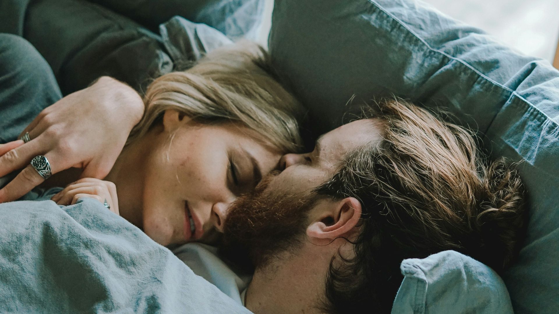 man kissing woman's forehead while lying on bed