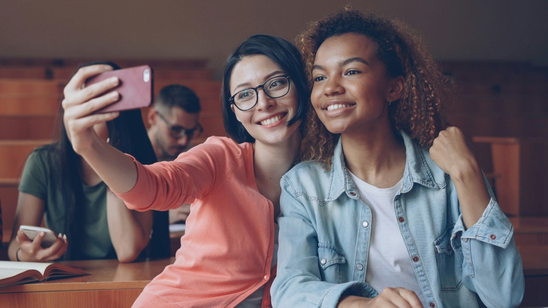 Two smiling students taking a selfie in a lecture hall.
