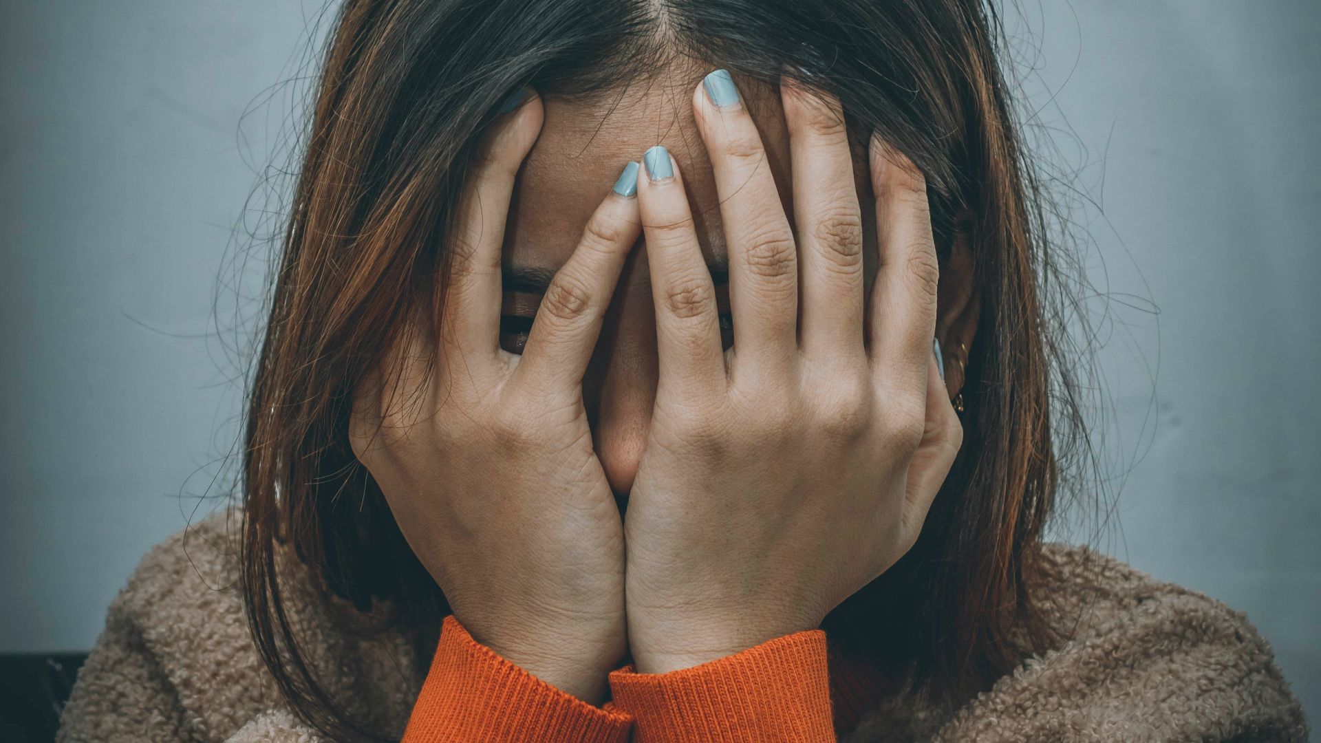 woman in brown sweater covering her face with her hand