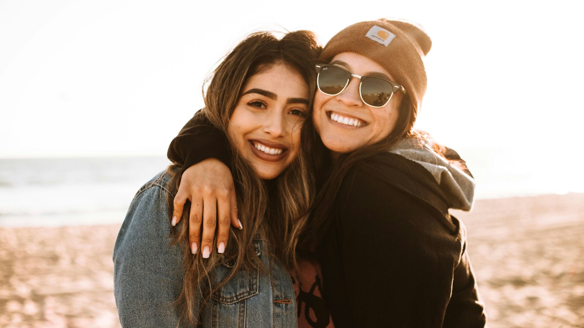 woman hugging other woman while smiling at beach