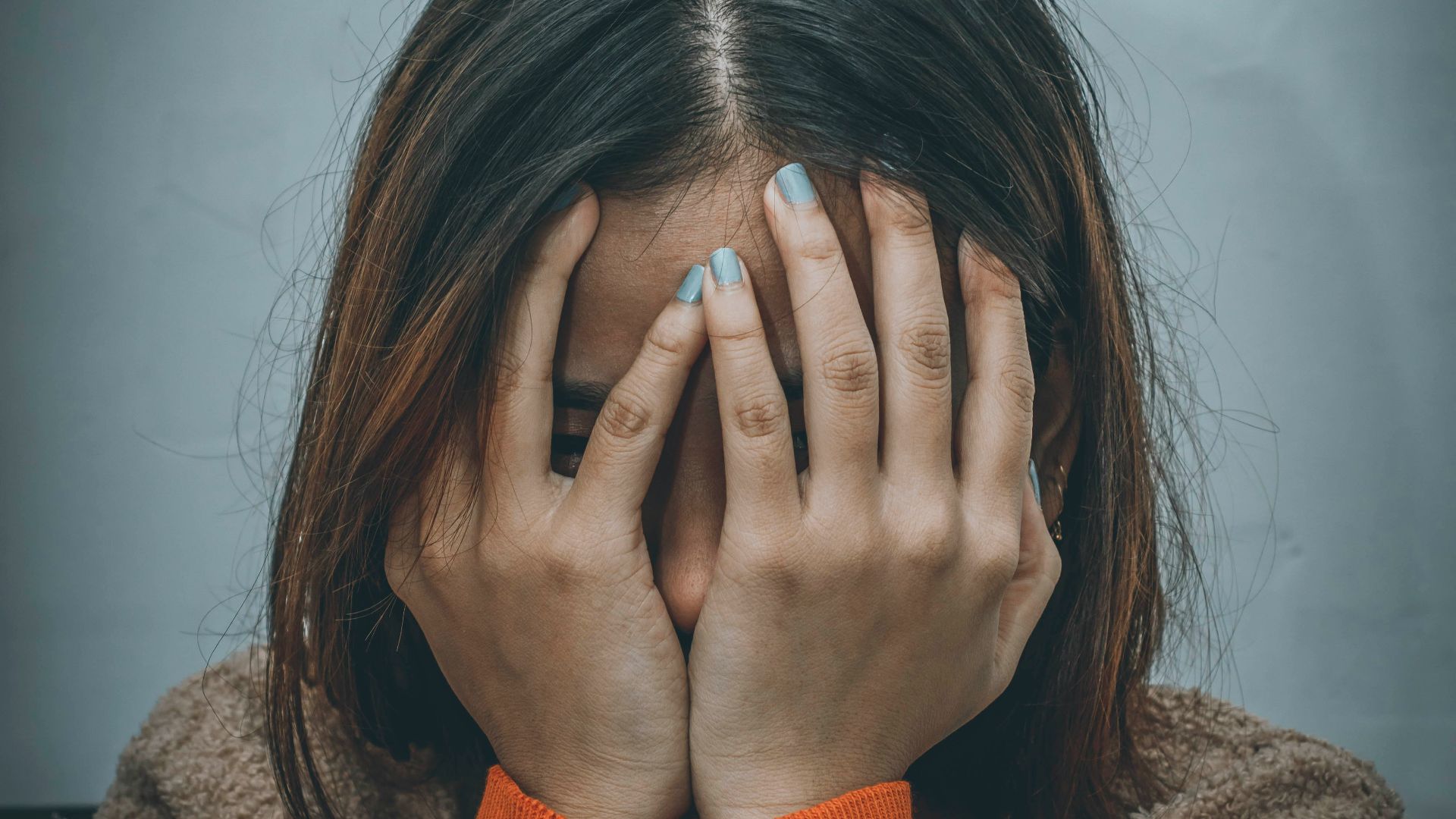woman in brown sweater covering her face with her hand