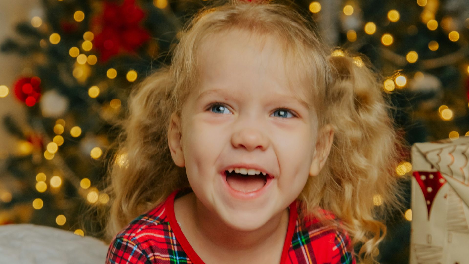 a little girl sitting in front of a christmas tree with presents