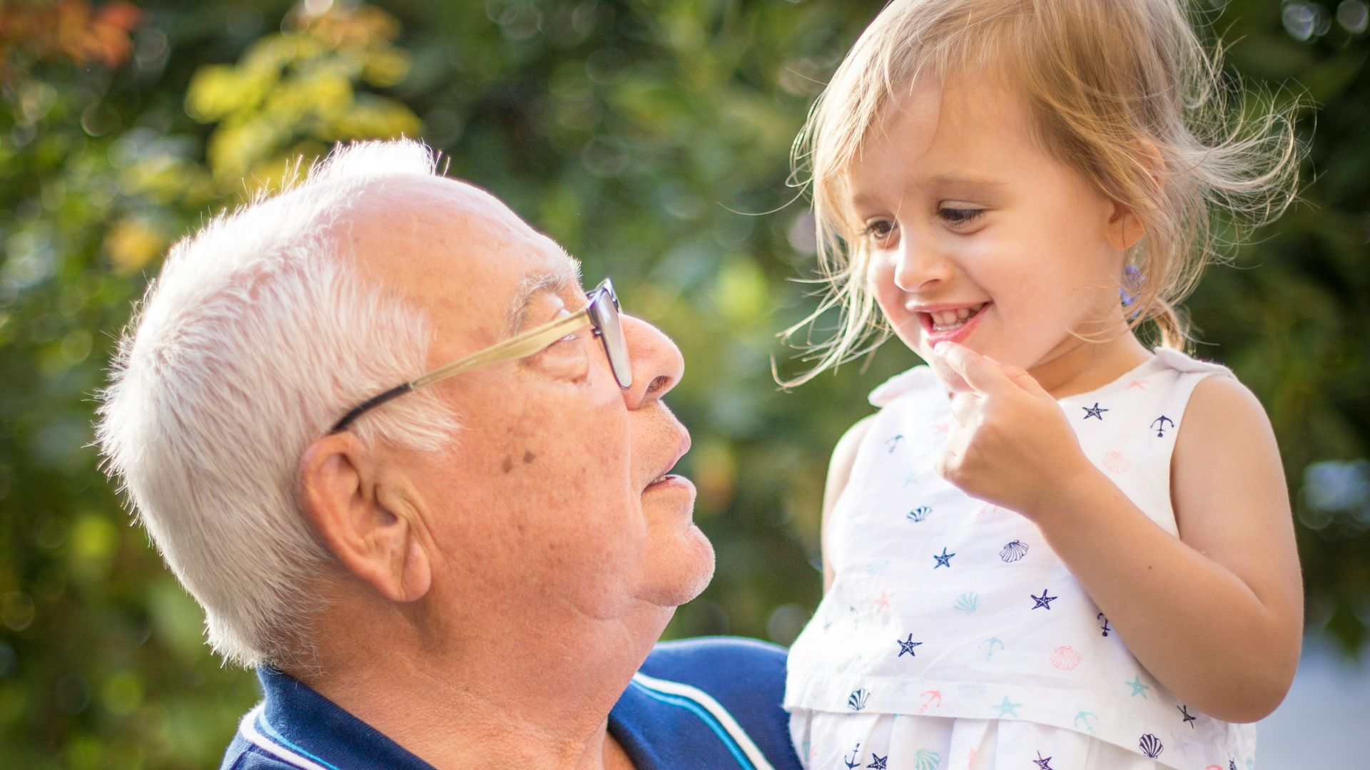 man in blue polo shirt carrying girl in white and pink floral dress