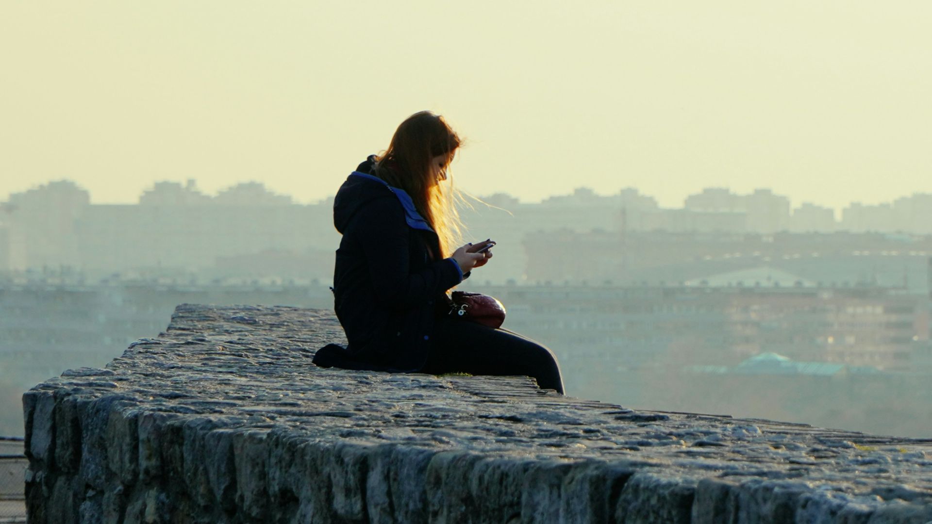 woman in black jacket sitting on gray concrete wall during daytime