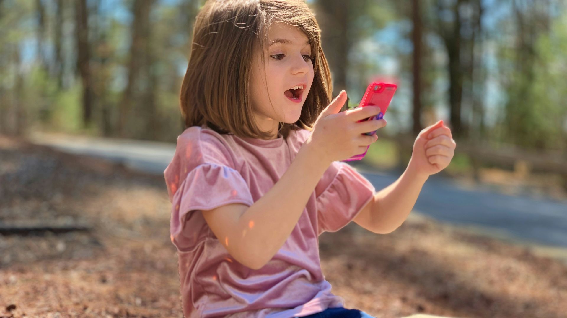 A little girl sitting on a bench using a cell phone