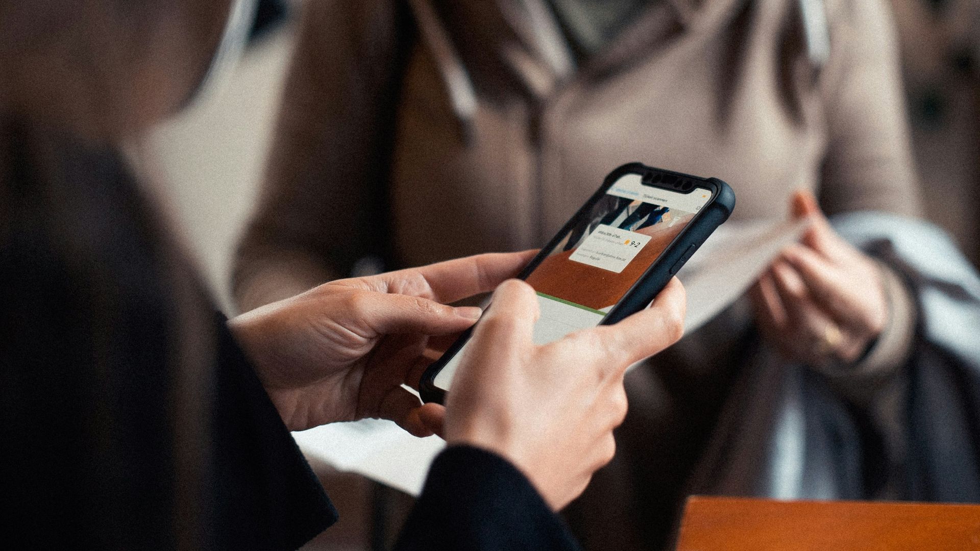woman in brown coat holding black smartphone
