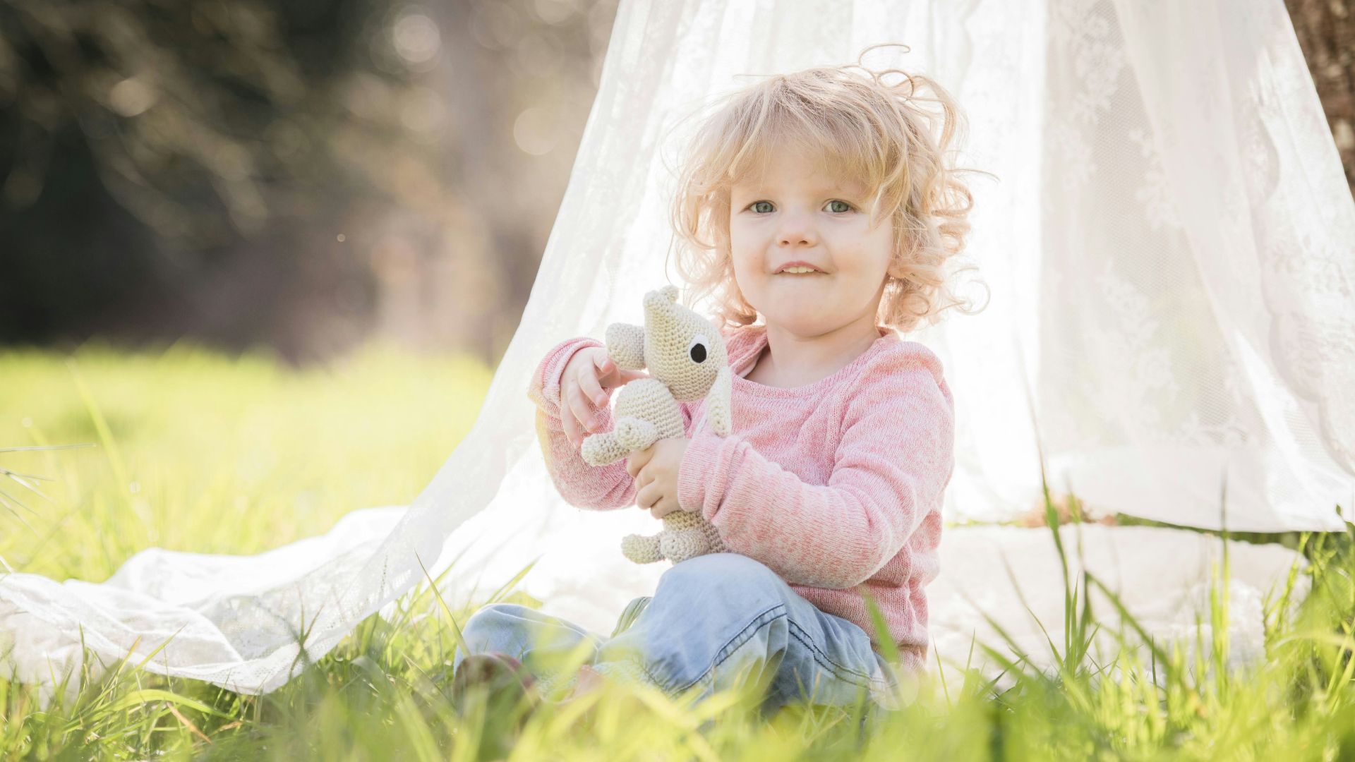 a little girl sitting in the grass with a stuffed animal