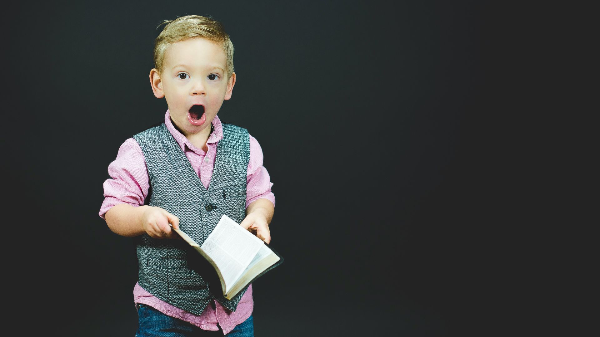 boy wearing gray vest and pink dress shirt holding book