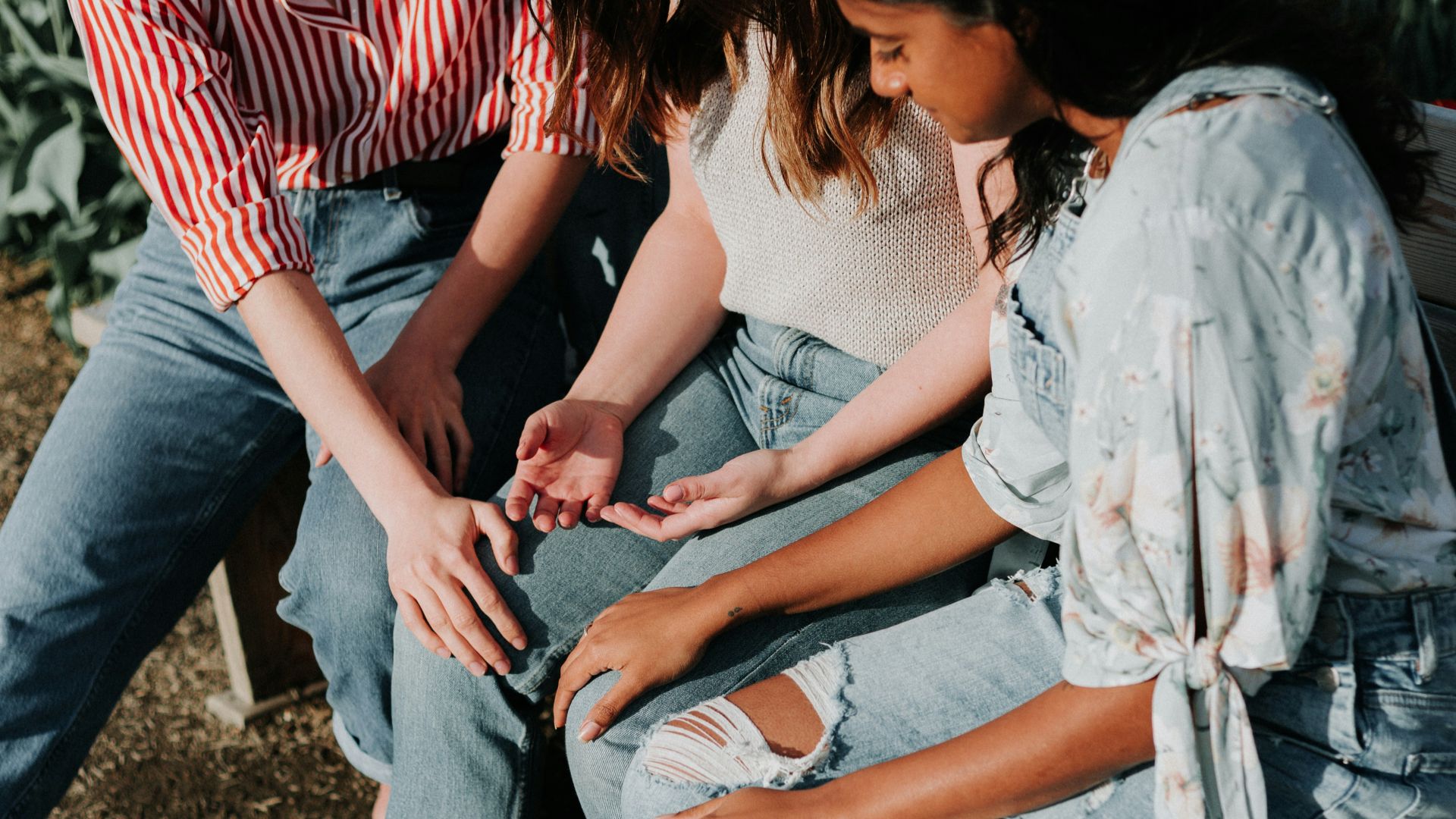 three women wearing blue denim jeans sitting on gray wooden bench