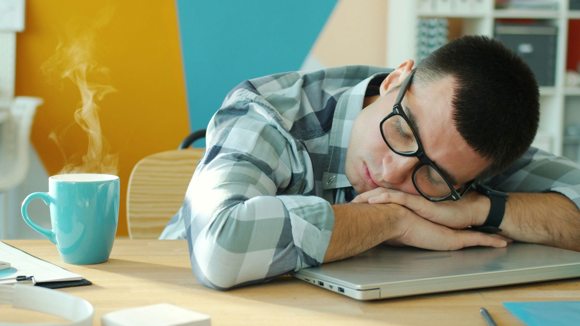Man sleeping at desk with coffee and laptop.