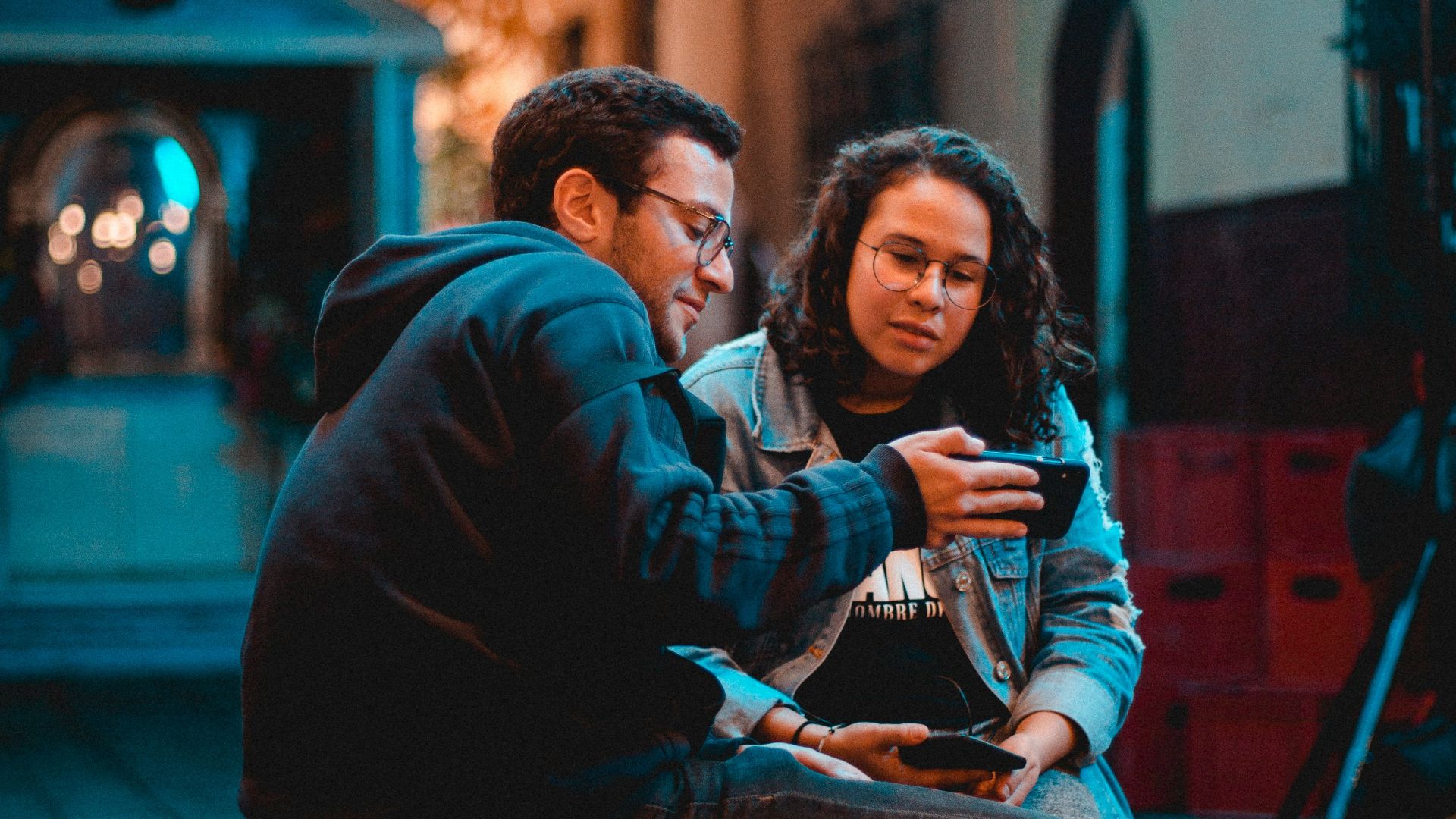 a man and woman sitting on a bench looking at a cell phone