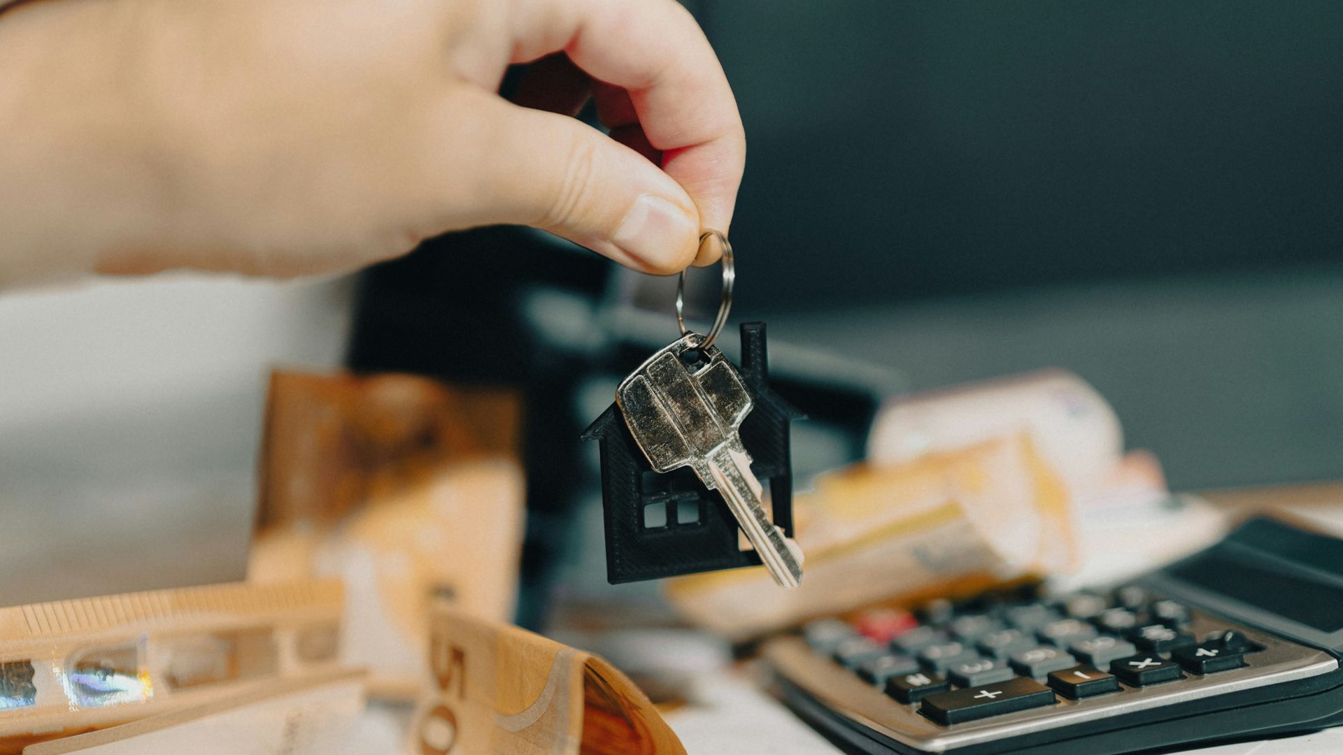 A person holding a house key in front of a calculator
