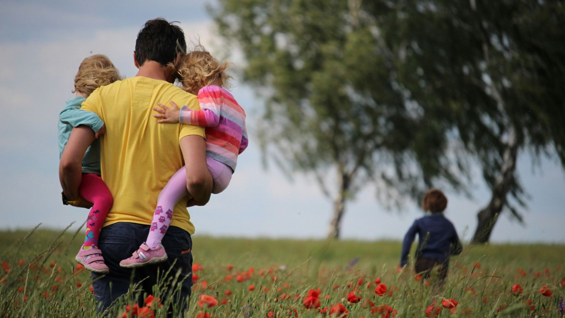 man carrying to girls on field of red petaled flower