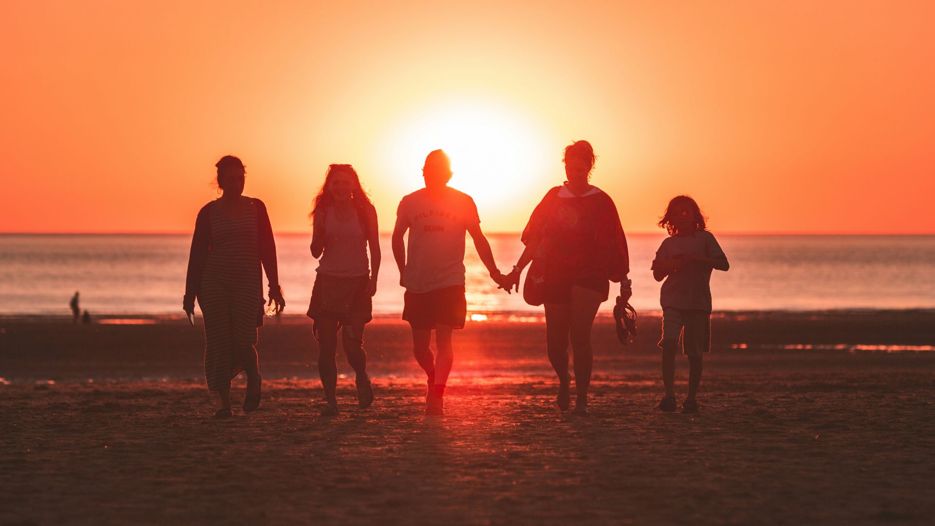 silhouette photo of five person walking on seashore during golden hour