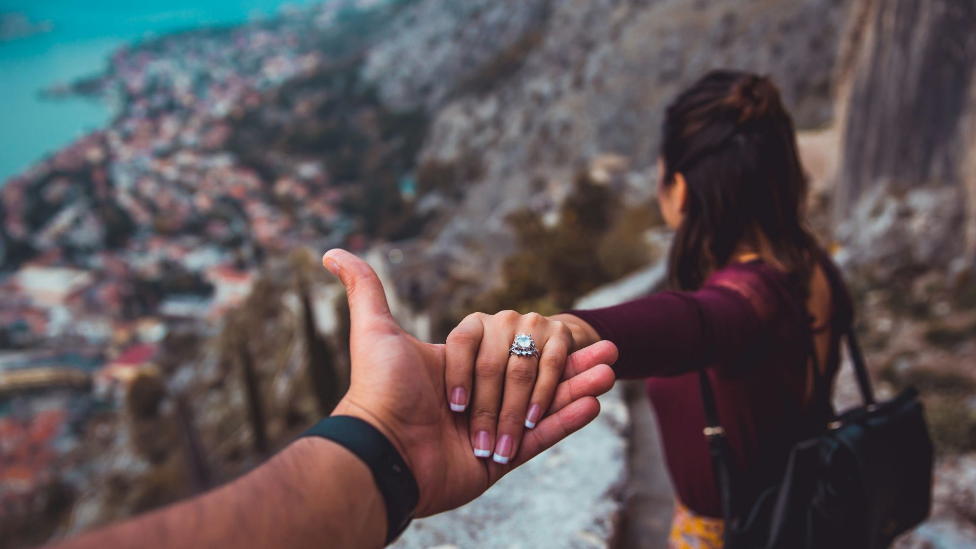 woman holding man's hand while looking on scenery of building beside body of water during daytime