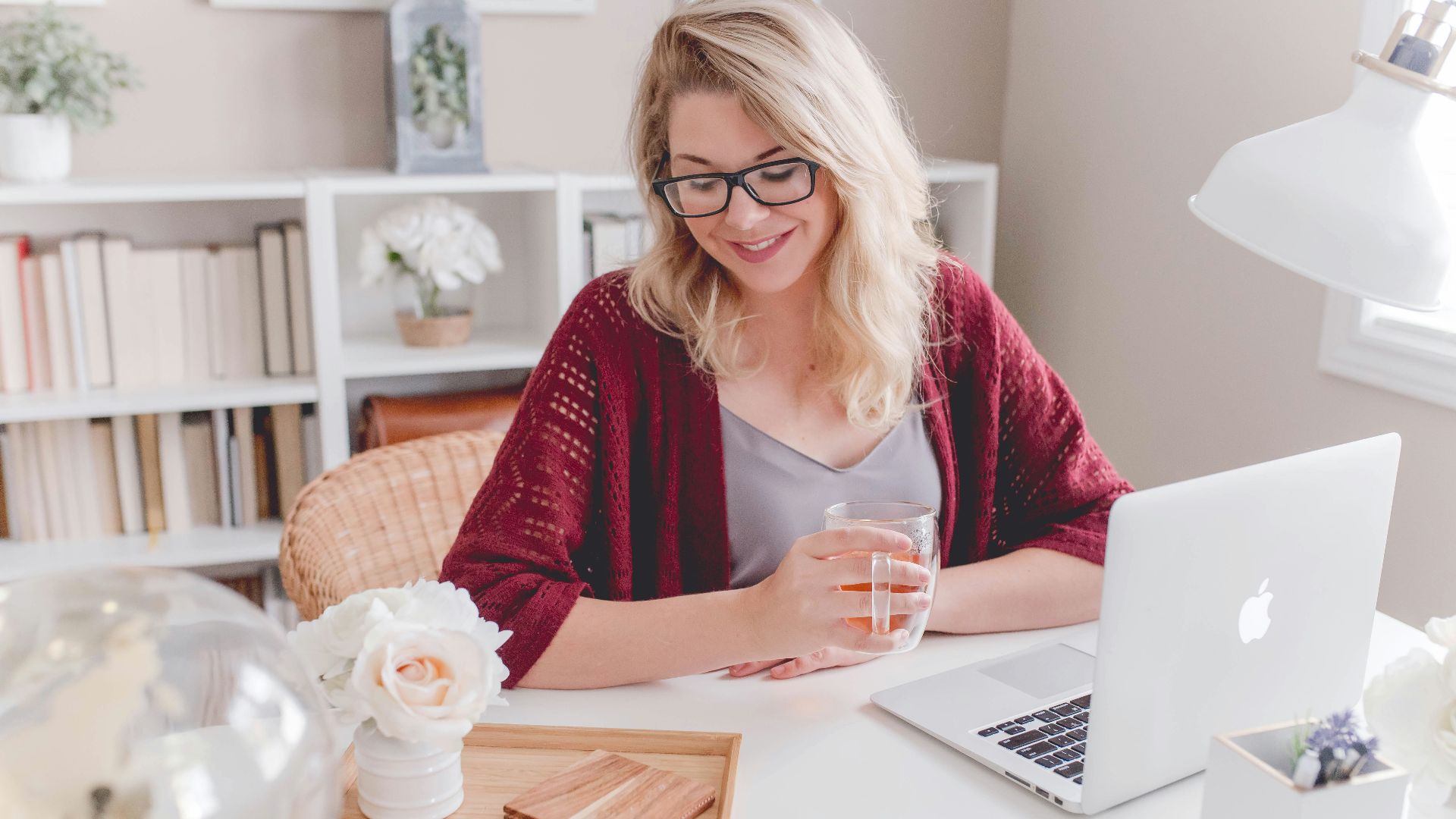 woman smiling holding glass mug sitting beside table with MacBook