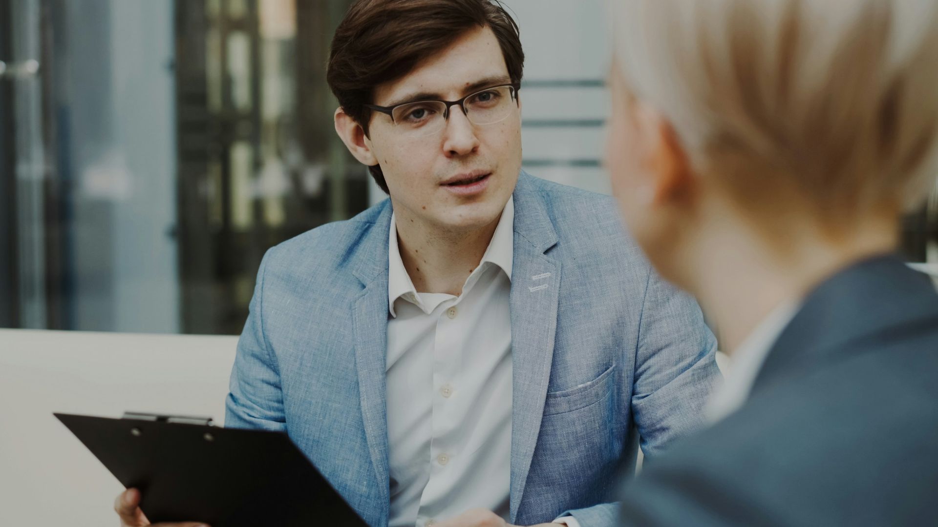 Man in suit holding clipboard talking to woman