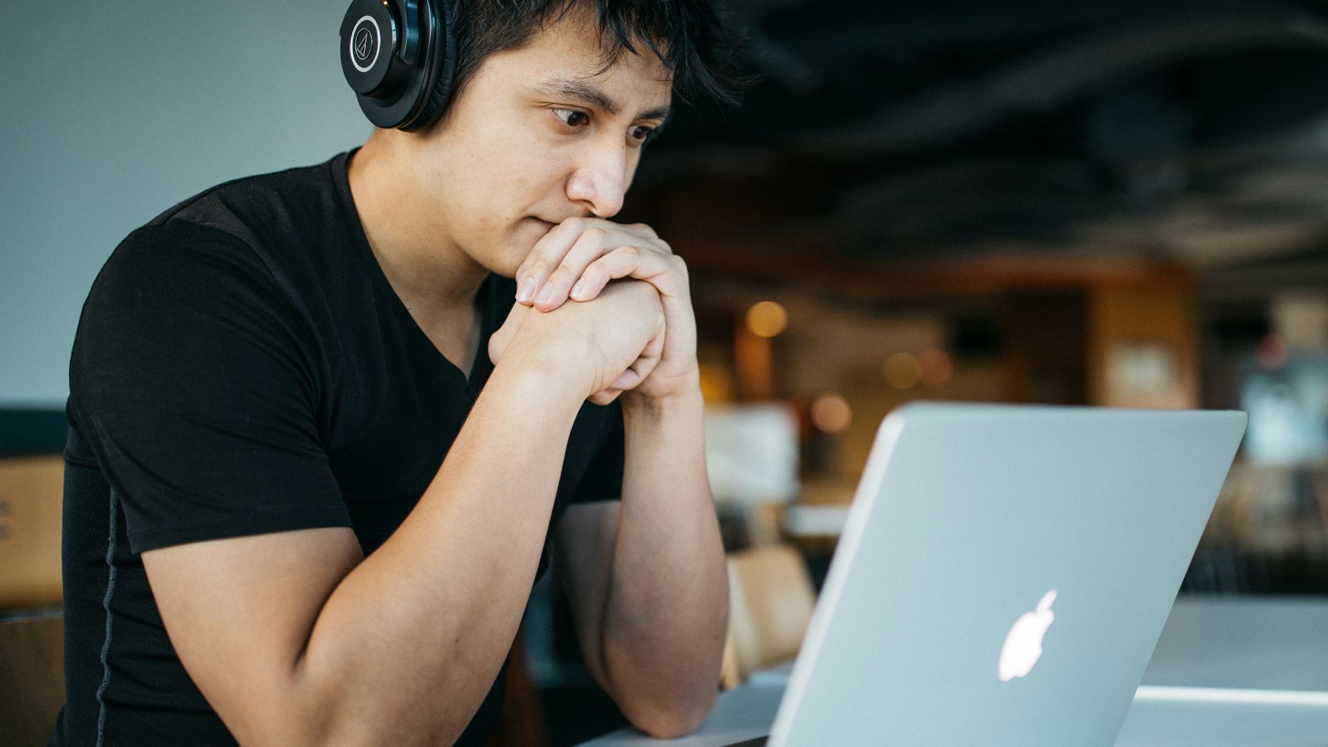 man wearing headphones while sitting on chair in front of MacBook