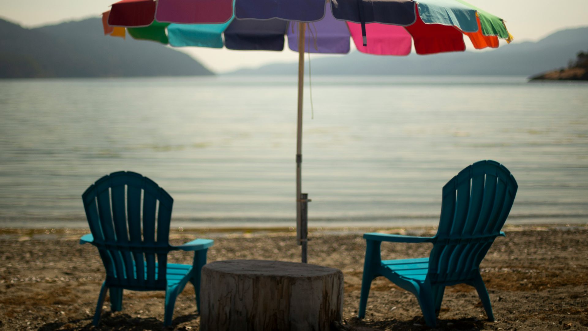 two blue lounge chairs under multicolored parasol in beach