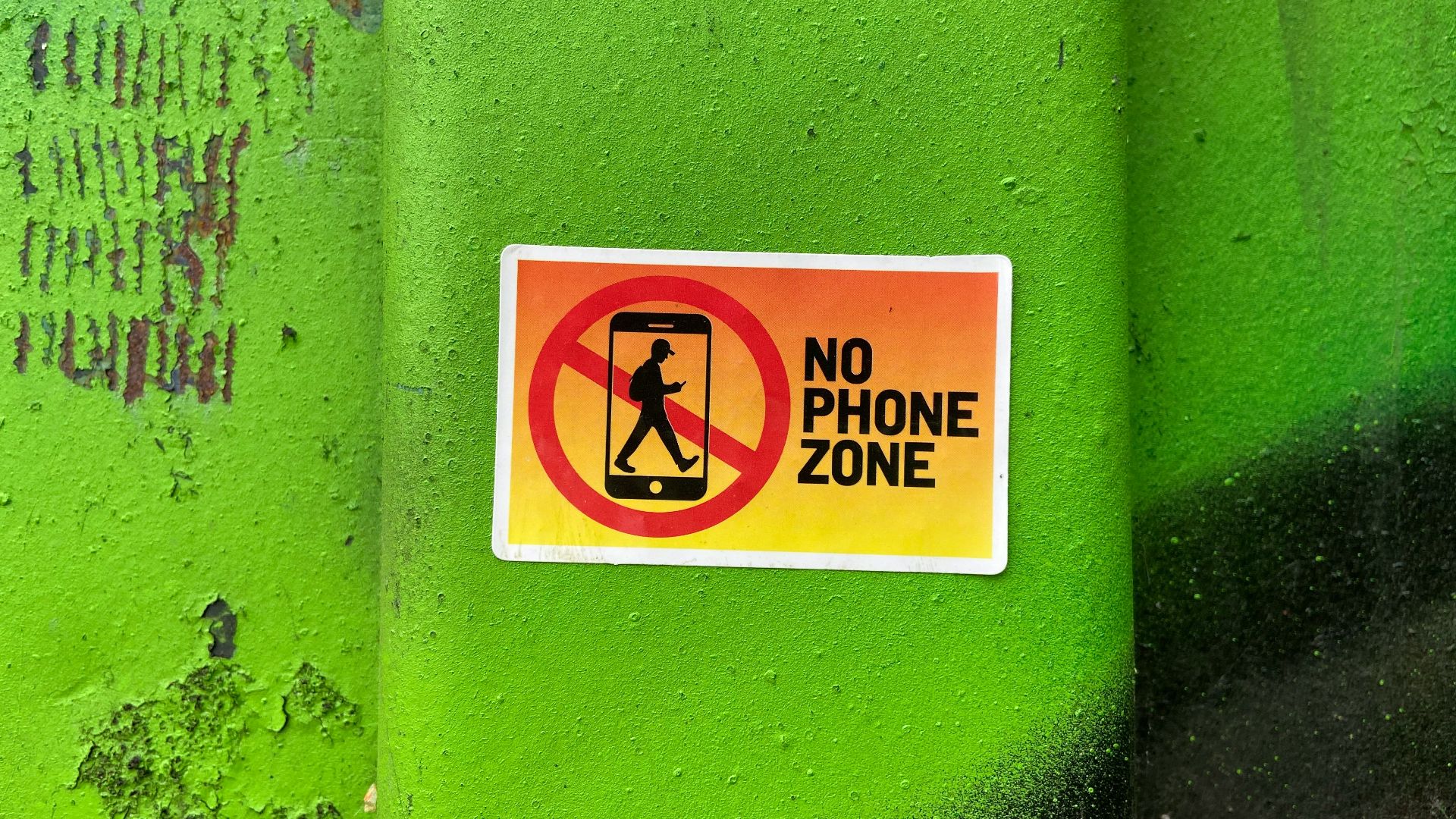 A no phone zone sign on a green wall