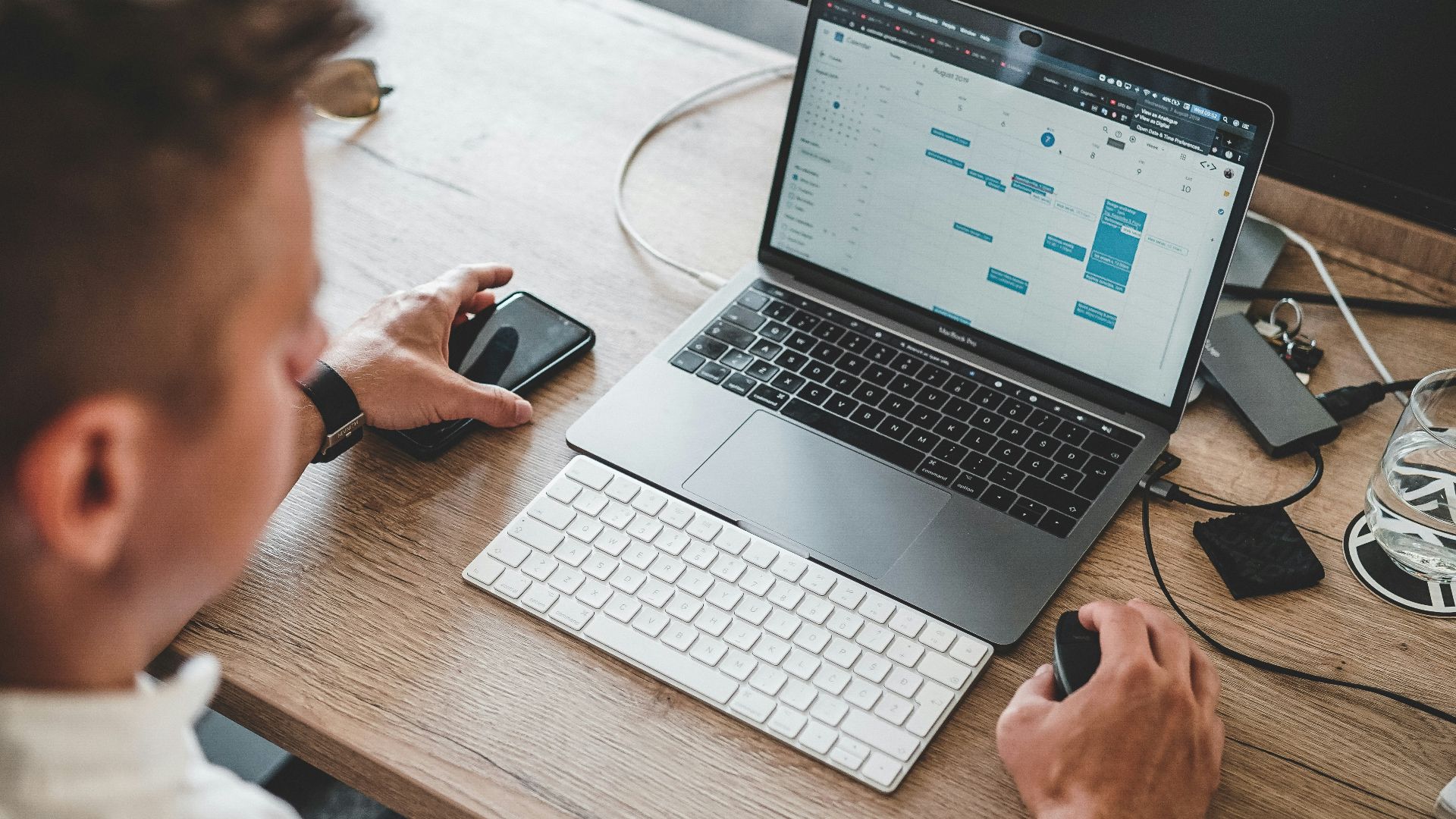 man holding mouse and iPhone while using Macbook Pro