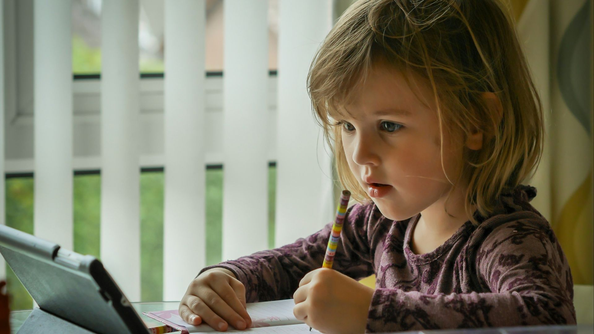 girl in purple and black long sleeve shirt holding black pen writing on white paper