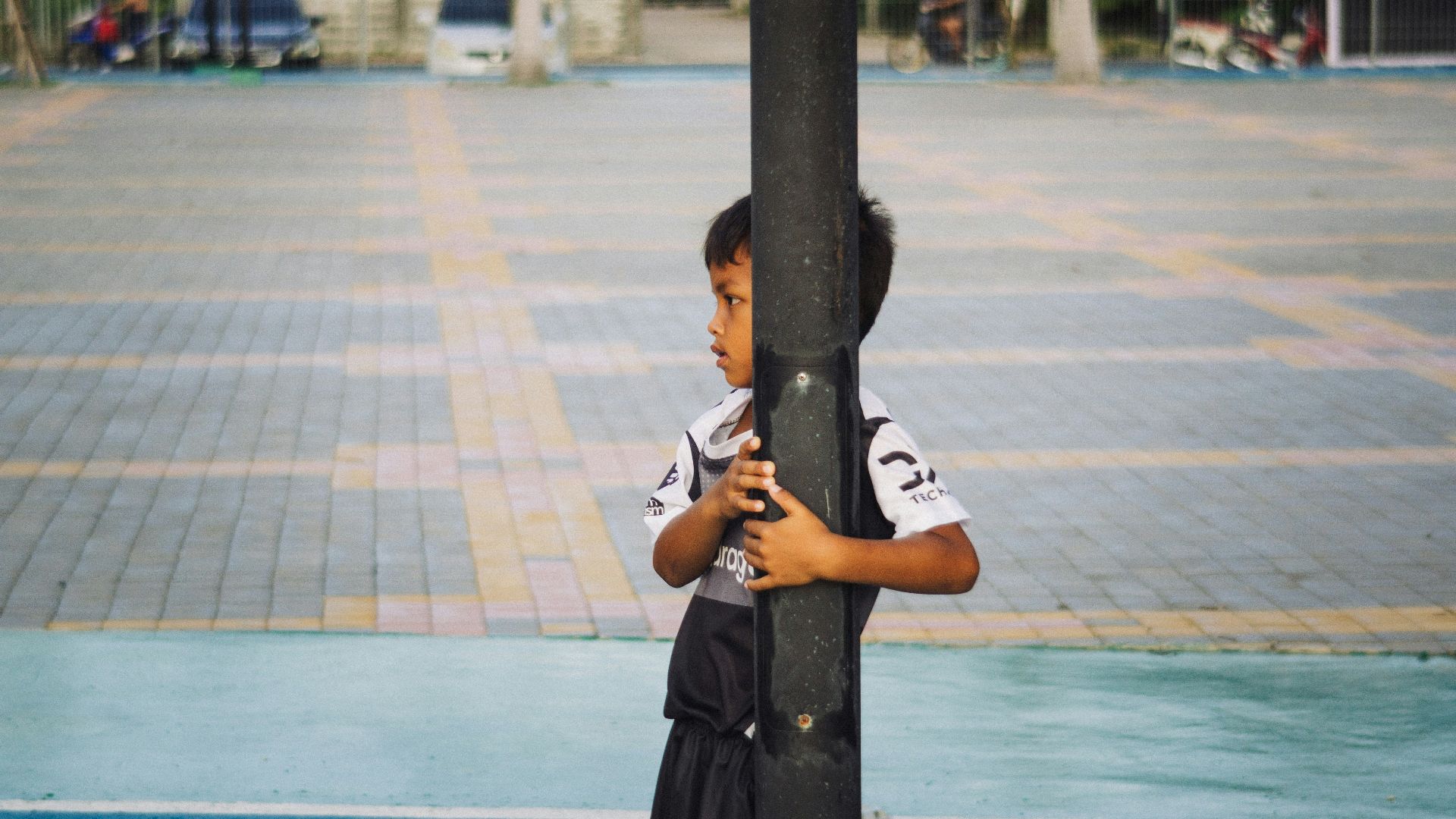 A boy hugs a pole, looking away.