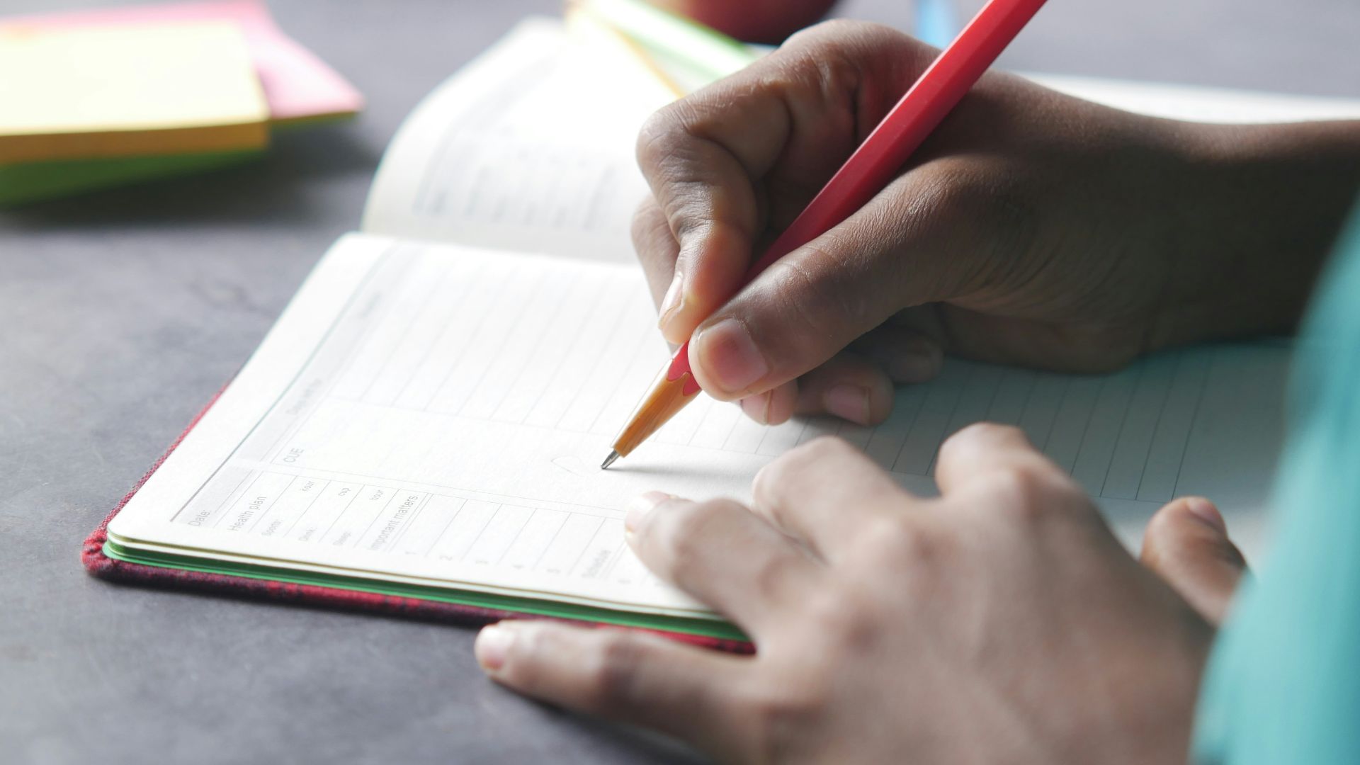 a person writing on a notebook with a pencil