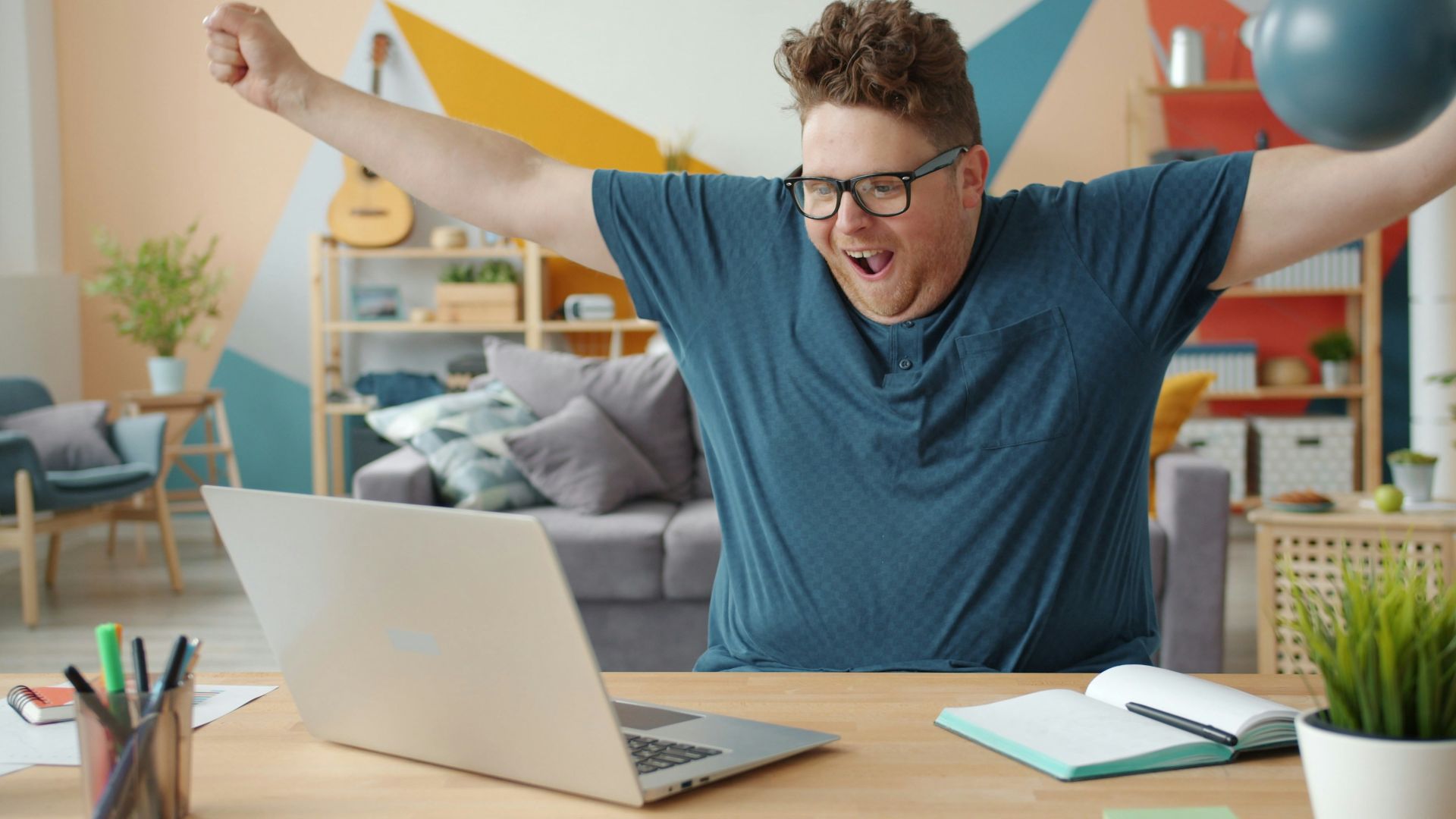 Man celebrating success while working on laptop at home.