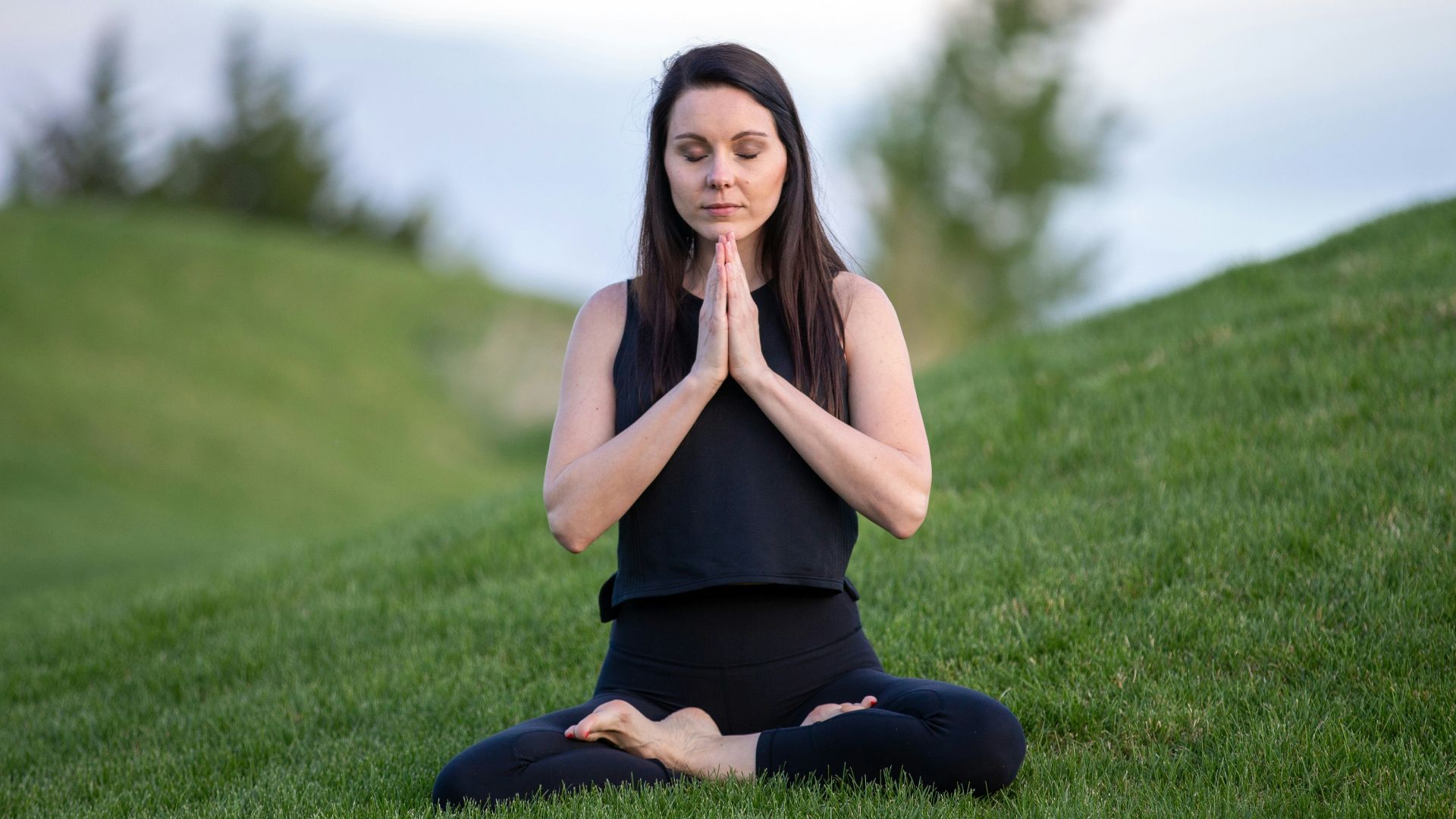 woman in black tank top and black pants sitting on green grass field during daytime