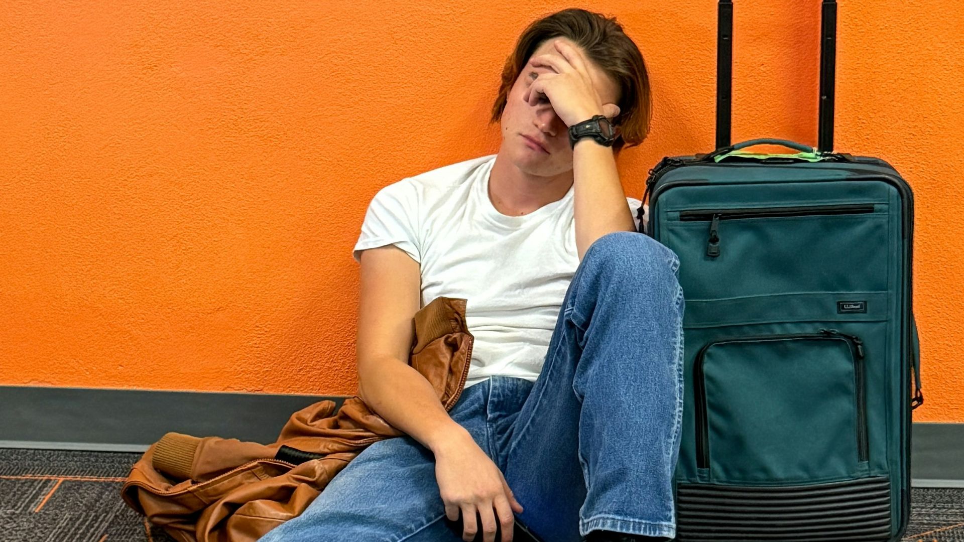 Man sitting on floor with luggage, looking tired.