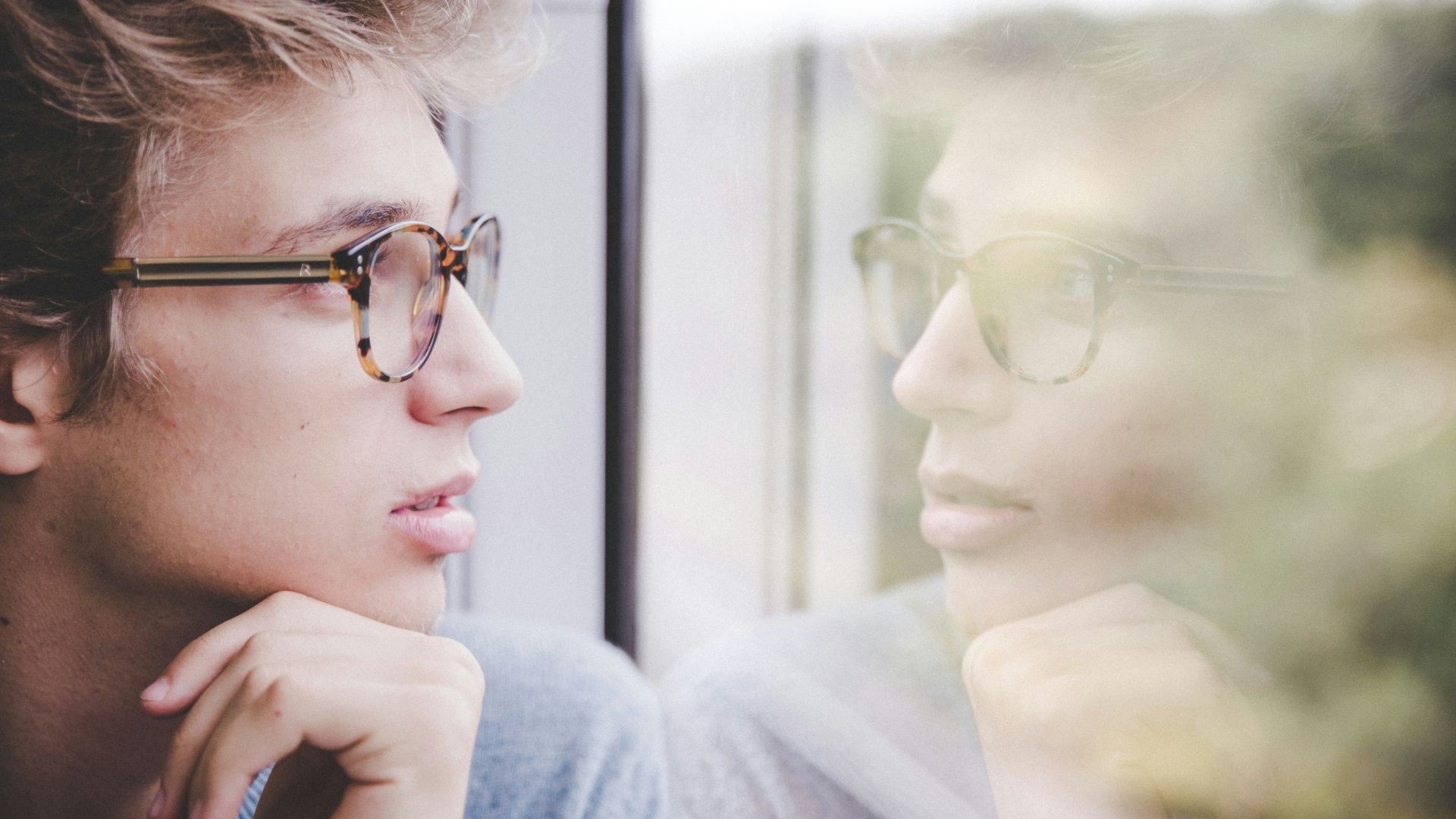 a man wearing glasses looking out a window