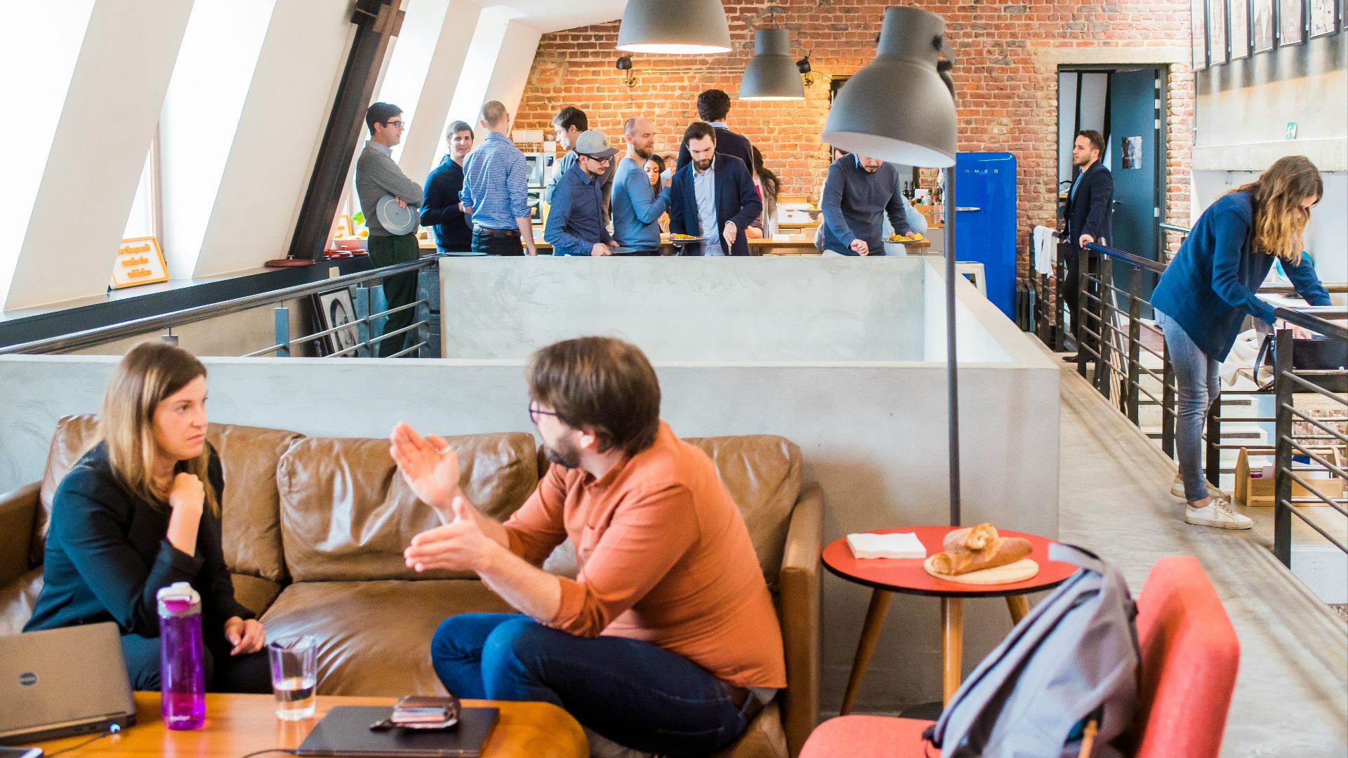 man in orange dress shirt talking and sitting in front of woman on brown sofa