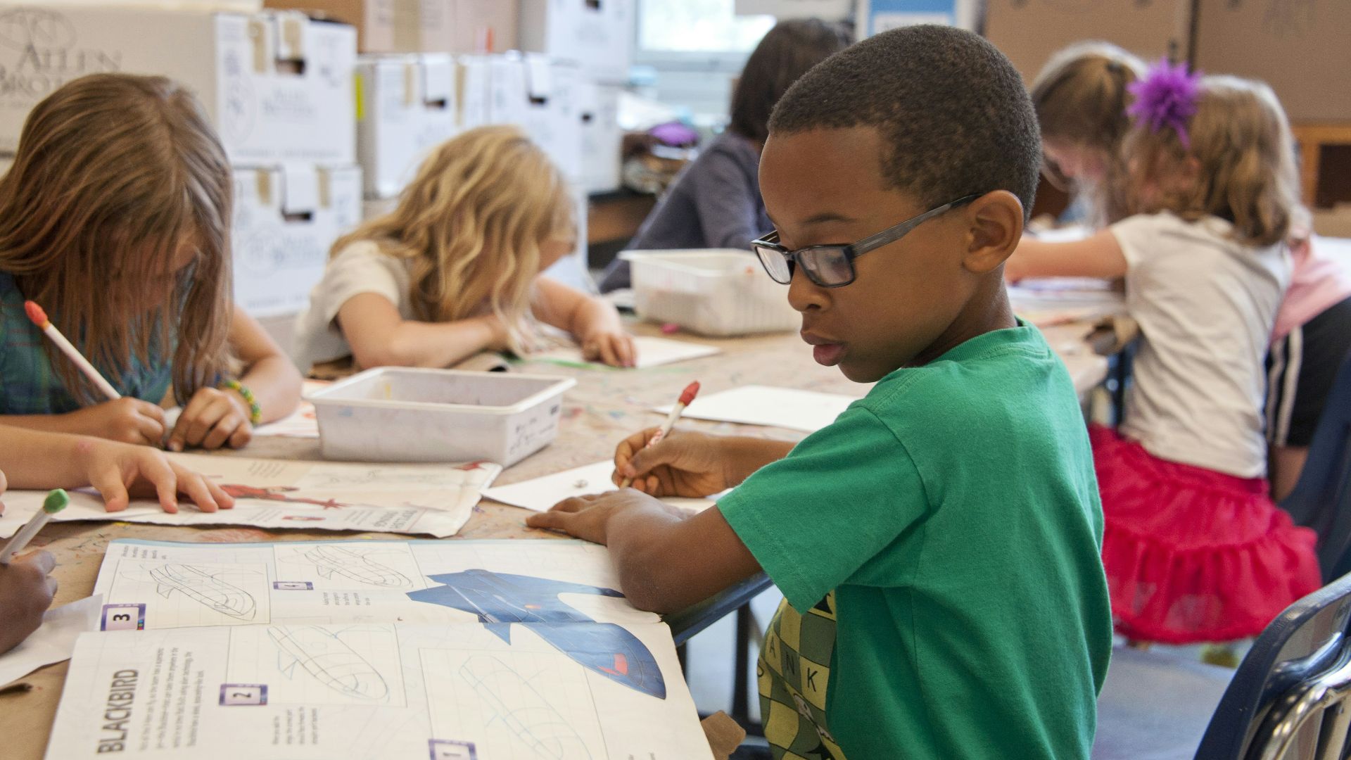 boy in green sweater writing on white paper