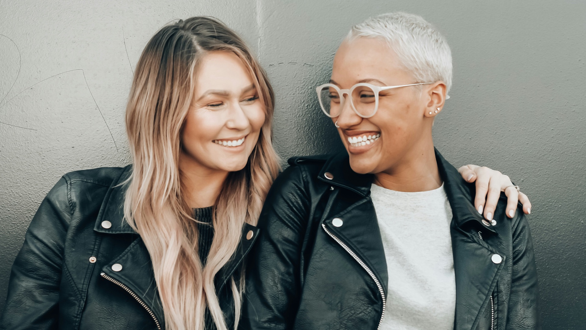 woman in black leather jacket beside woman in gray shirt