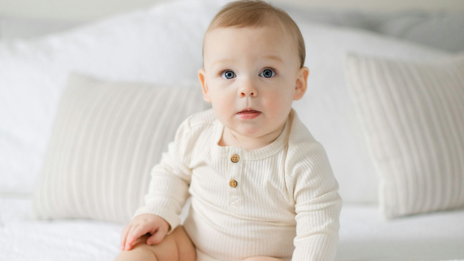 a baby sitting on a bed with white sheets
