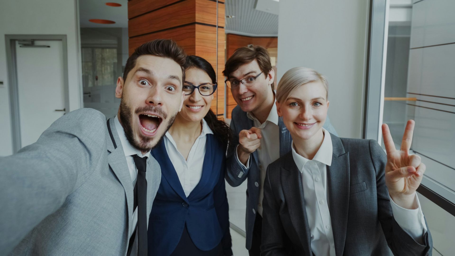 Four colleagues taking a selfie in an office hallway.