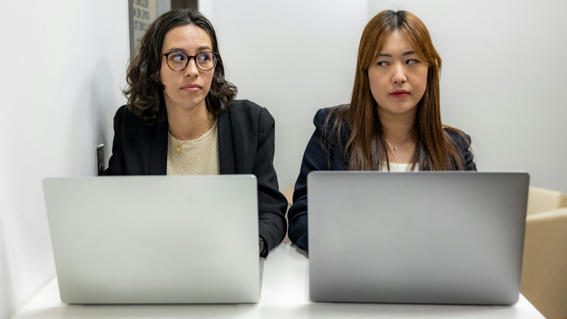 two women sitting at a table with laptops