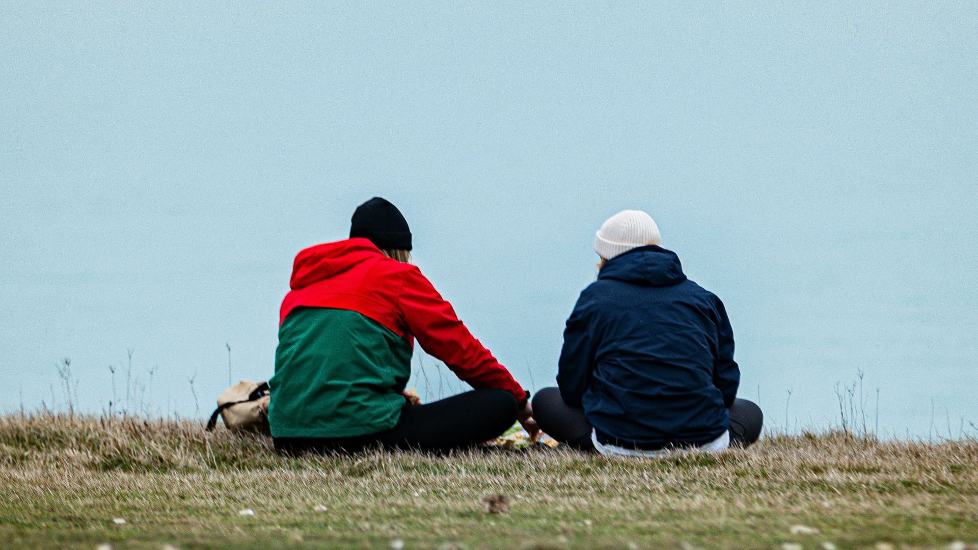 a couple of people sitting on top of a grass covered field