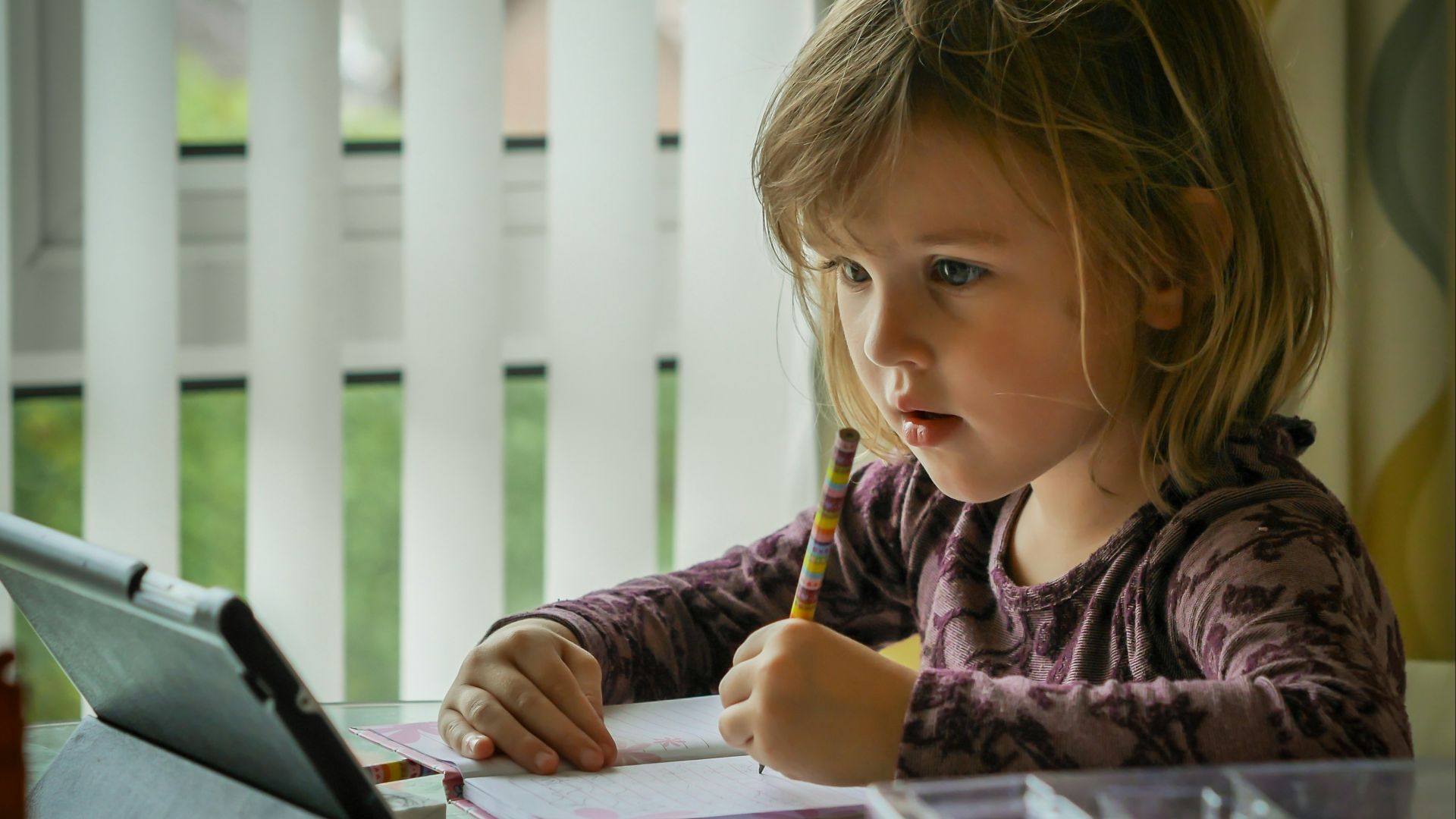 girl in purple and black long sleeve shirt holding black pen writing on white paper