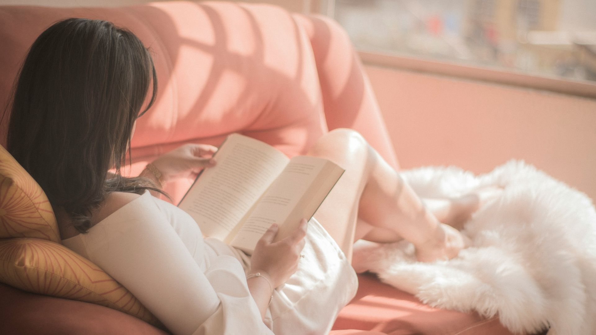 woman holding book sitting on pink fabric sofa
