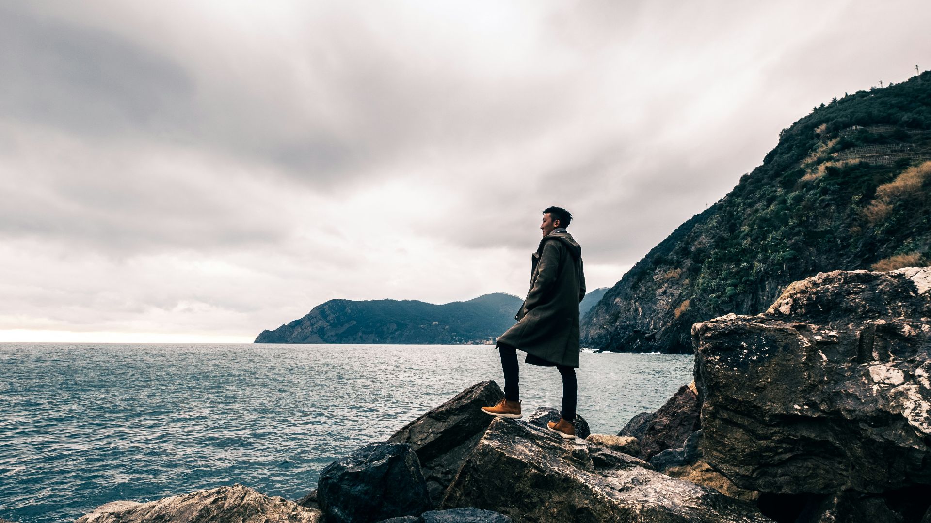 man standing on boulder near body of water